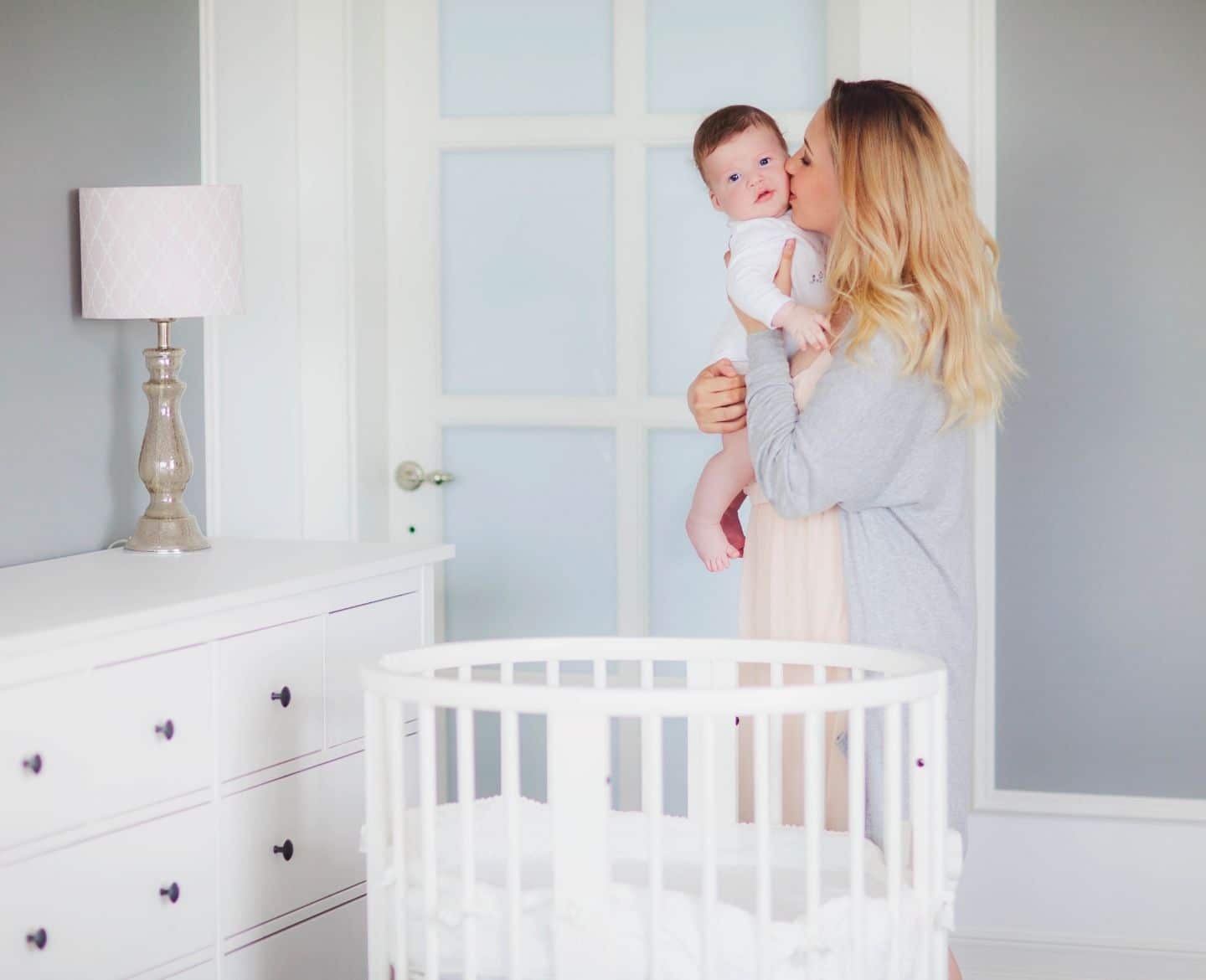 woman kissing baby on the cheek standing over a crib