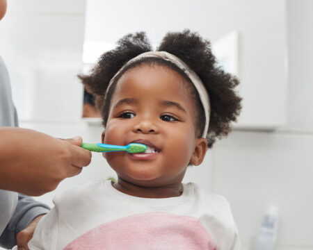 mom helping her toddler daughter brush her teeth