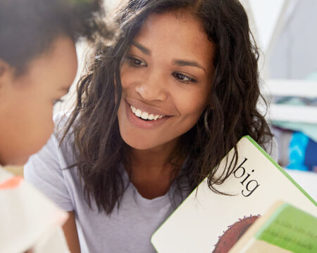 mom smiling at her toddler while she holds a book